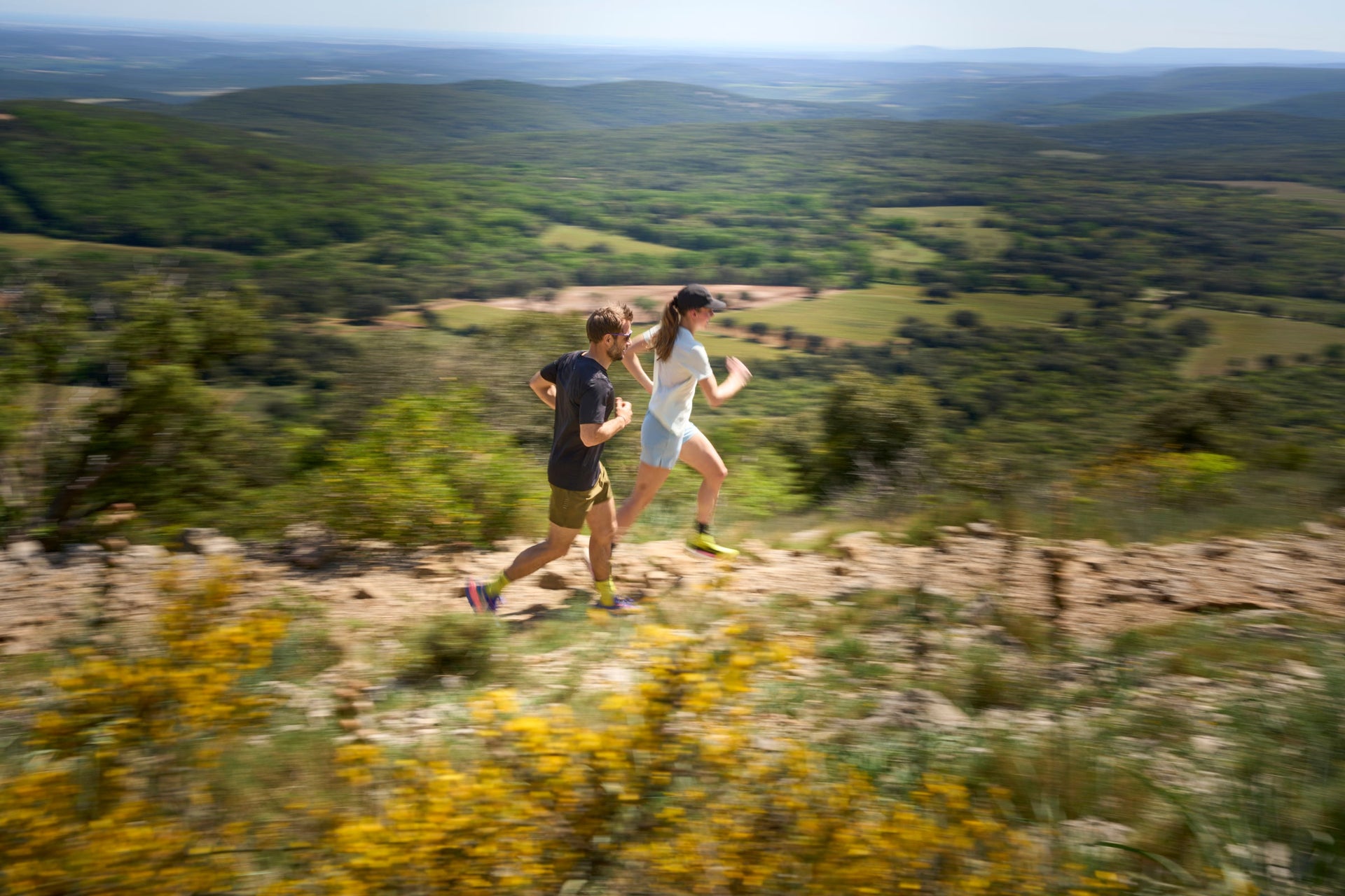 Two people running on a trail with a scenic landscape in the background
