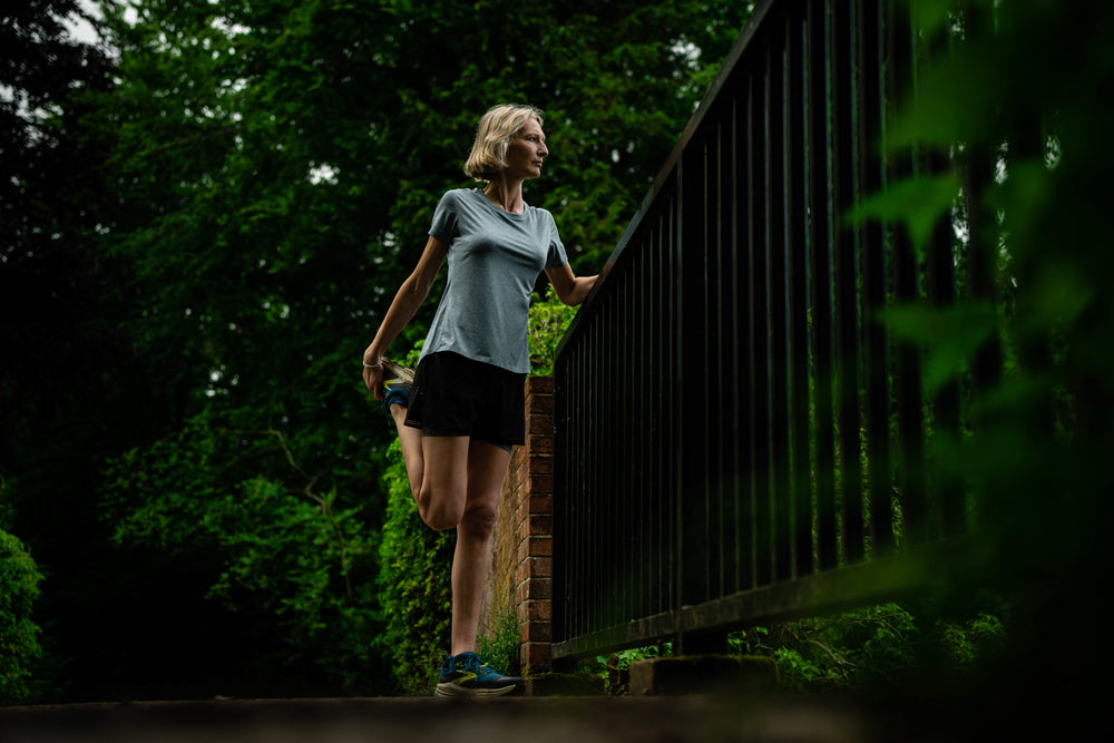A woman in Flyte athletic wear standing and leaning on a bridge railing in a lush green park