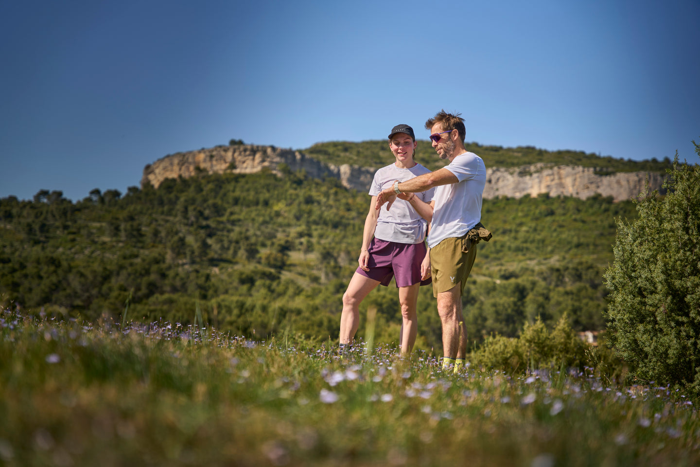 Two people standing in a grassy field with mountains in the background