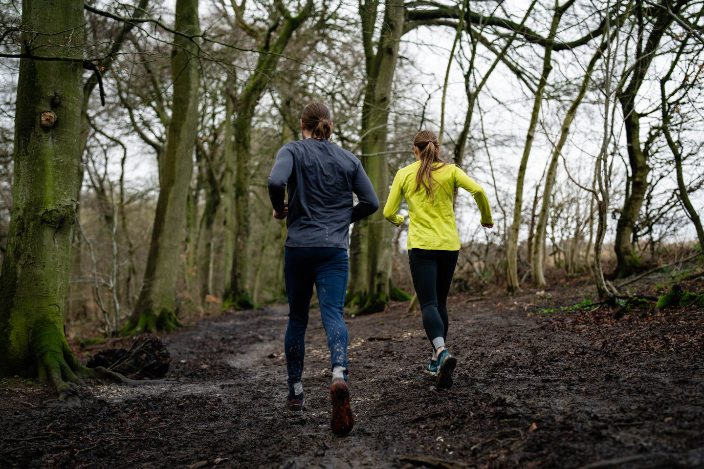 Two people running on a muddy forest trail