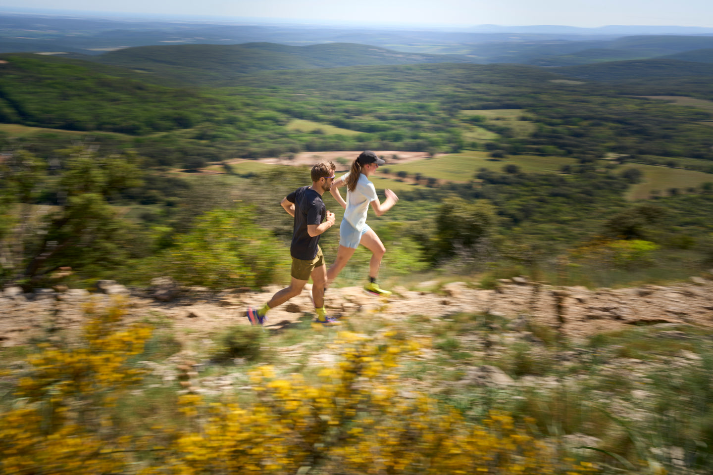 Two people running on a trail with a scenic landscape in the background