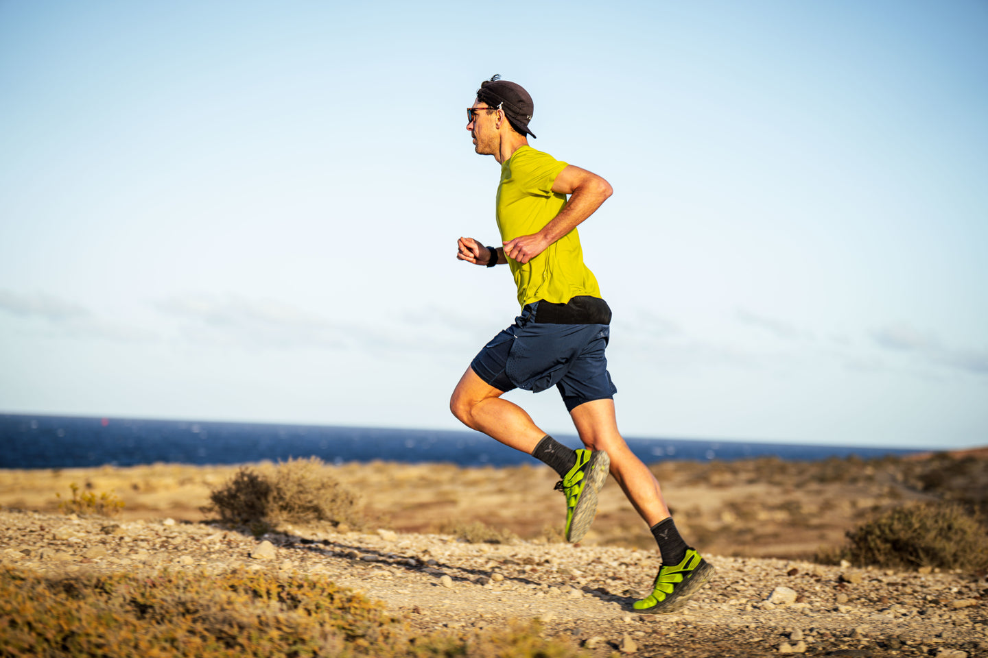Man running on a trail with a clear sky and ocean in the background
