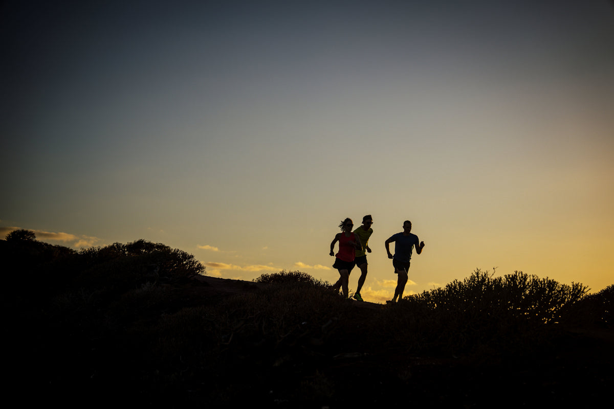 Three people running on a hill at sunset