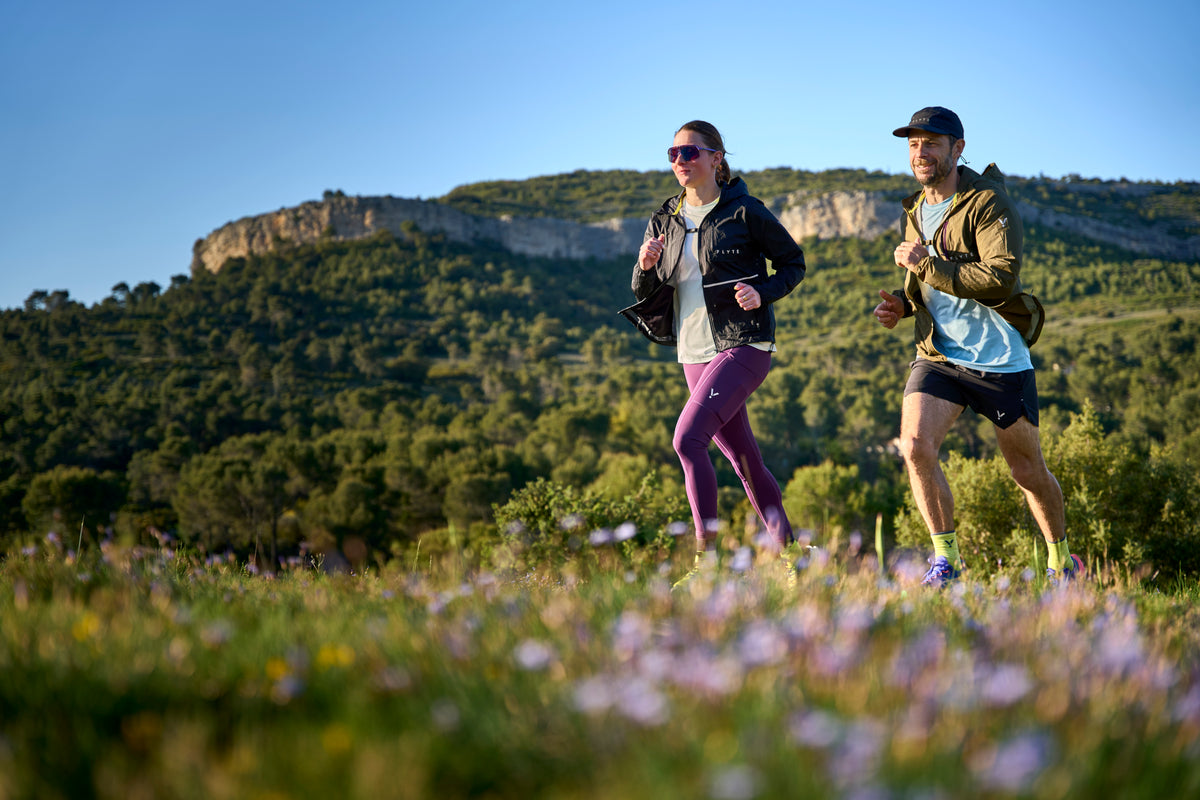 Two people running on a grassy hill with mountains in the background